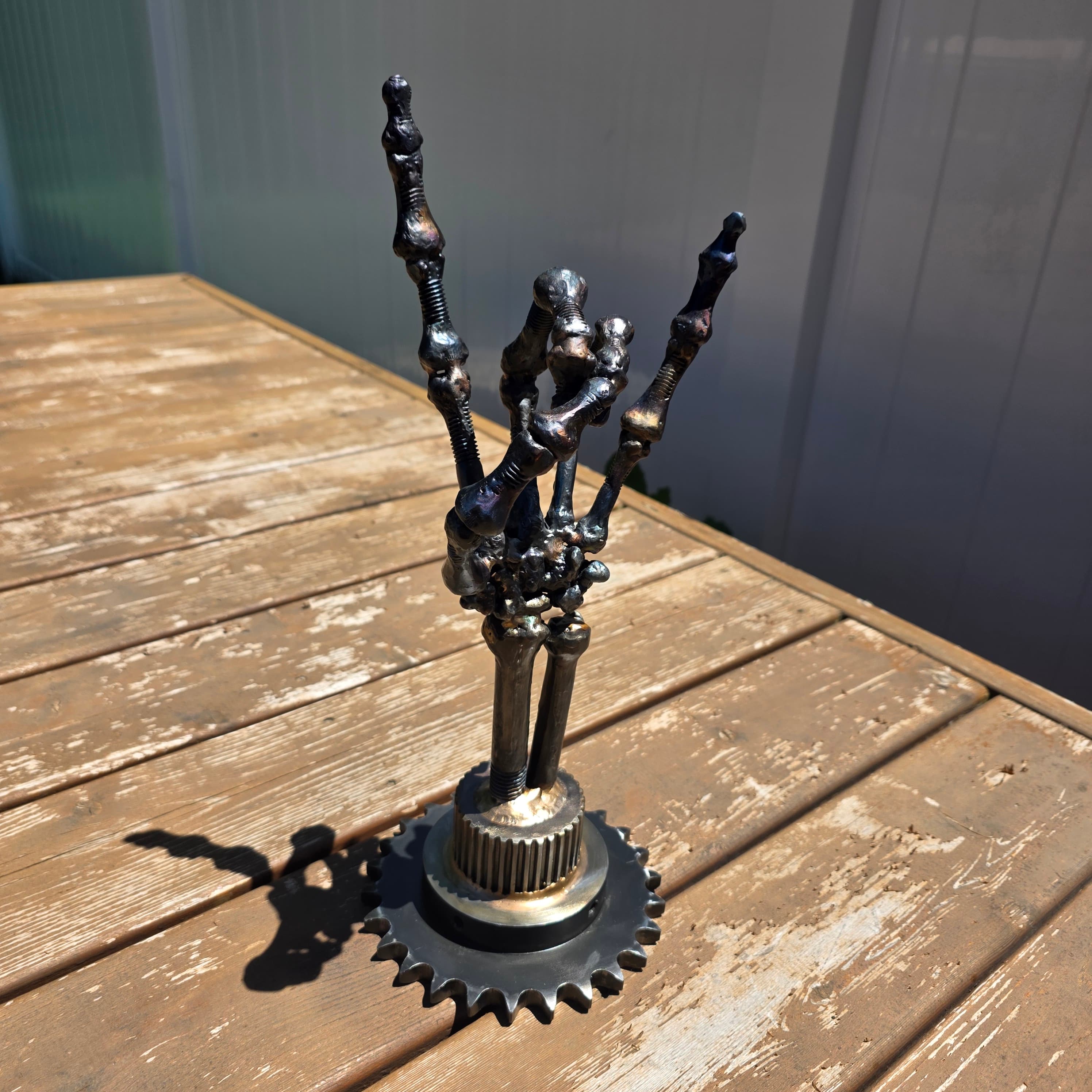 Hand-forged metal sculpture of a hand making the rock horns gesture by local artist Leah Reichwaldt, mounted on weathered wood